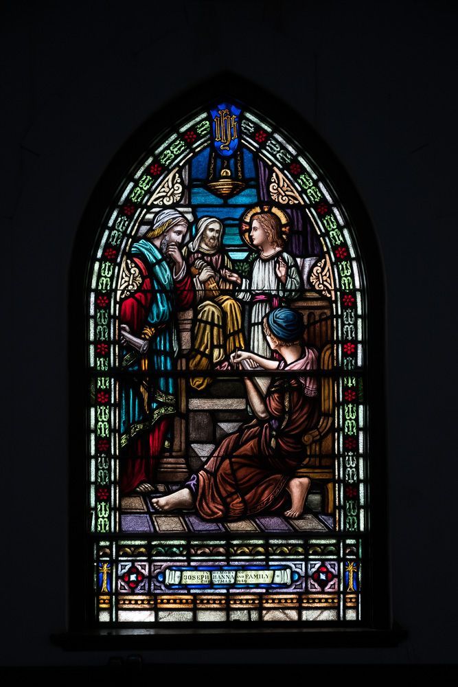 A stained glass window in a church shows a group of people standing around a table.