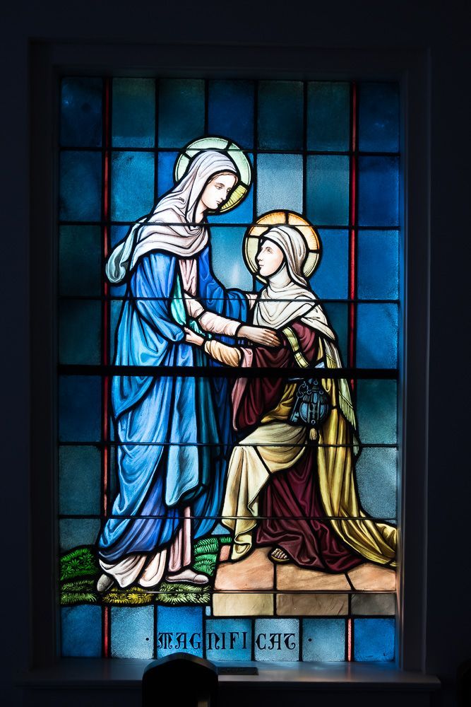 A stained glass window shows two women shaking hands.