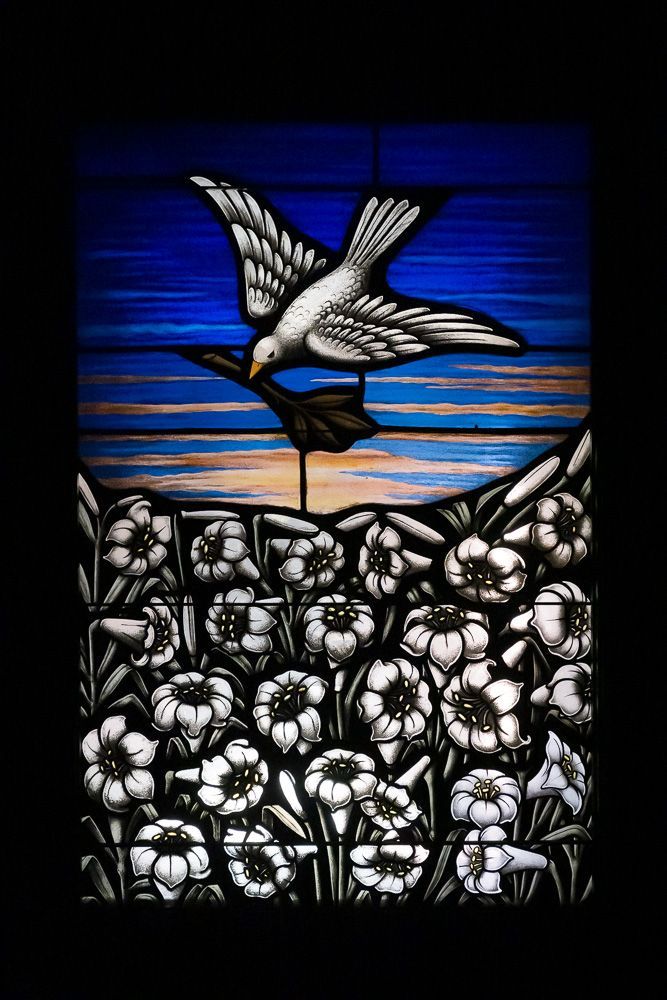 A stained glass window with a bird flying over a field of flowers.