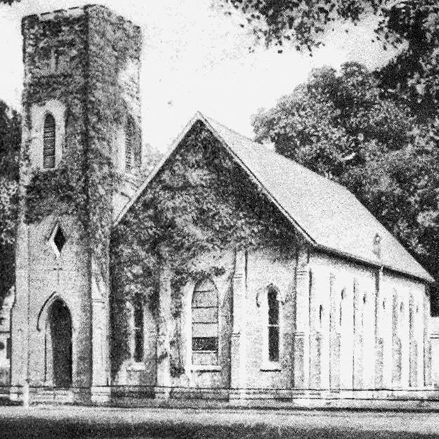 A black and white photo of a church with a tower surrounded by trees.