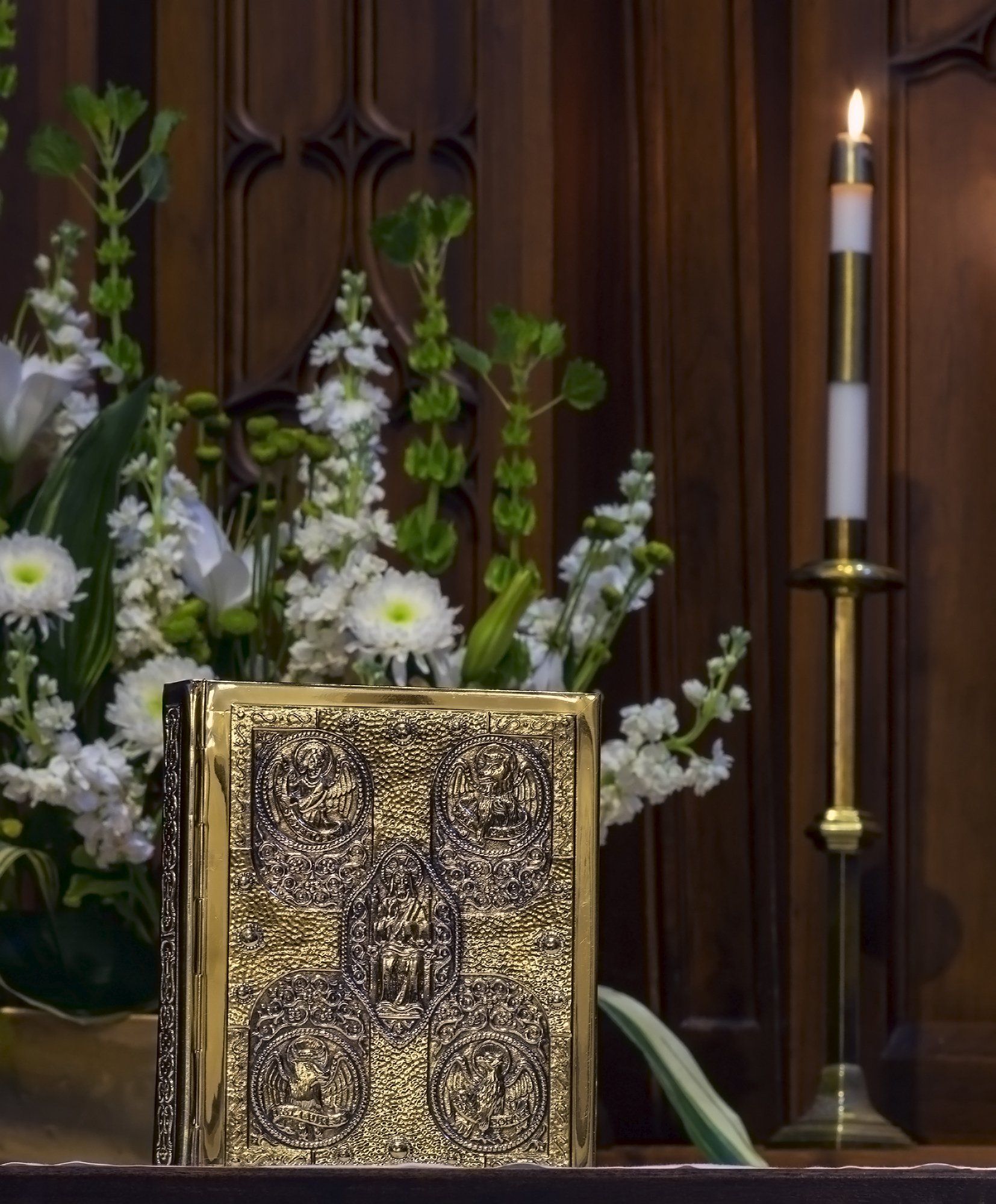 A candle is lit in front of a bible and flowers
