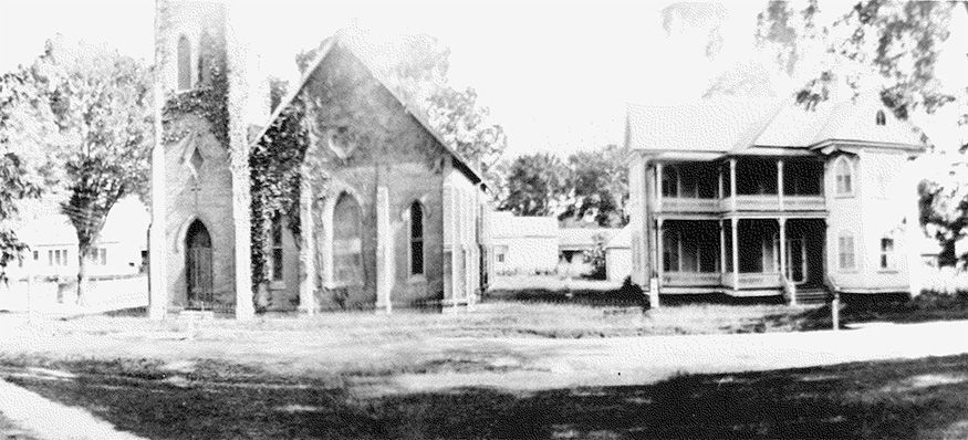 A black and white photo of a church and a house.