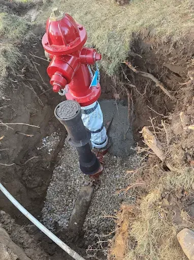 A red fire hydrant installed in an open dirt trench, with its base wrapped in white material and a valve box nearby.