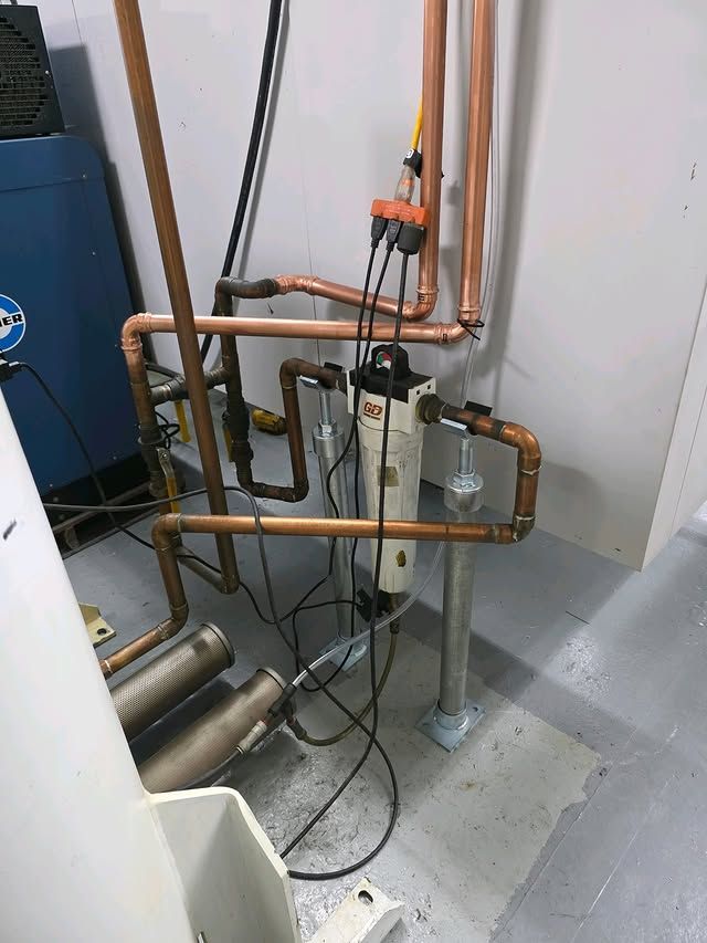 Copper plumbing pipes and a white filtration unit installed against a white wall in an industrial utility room.