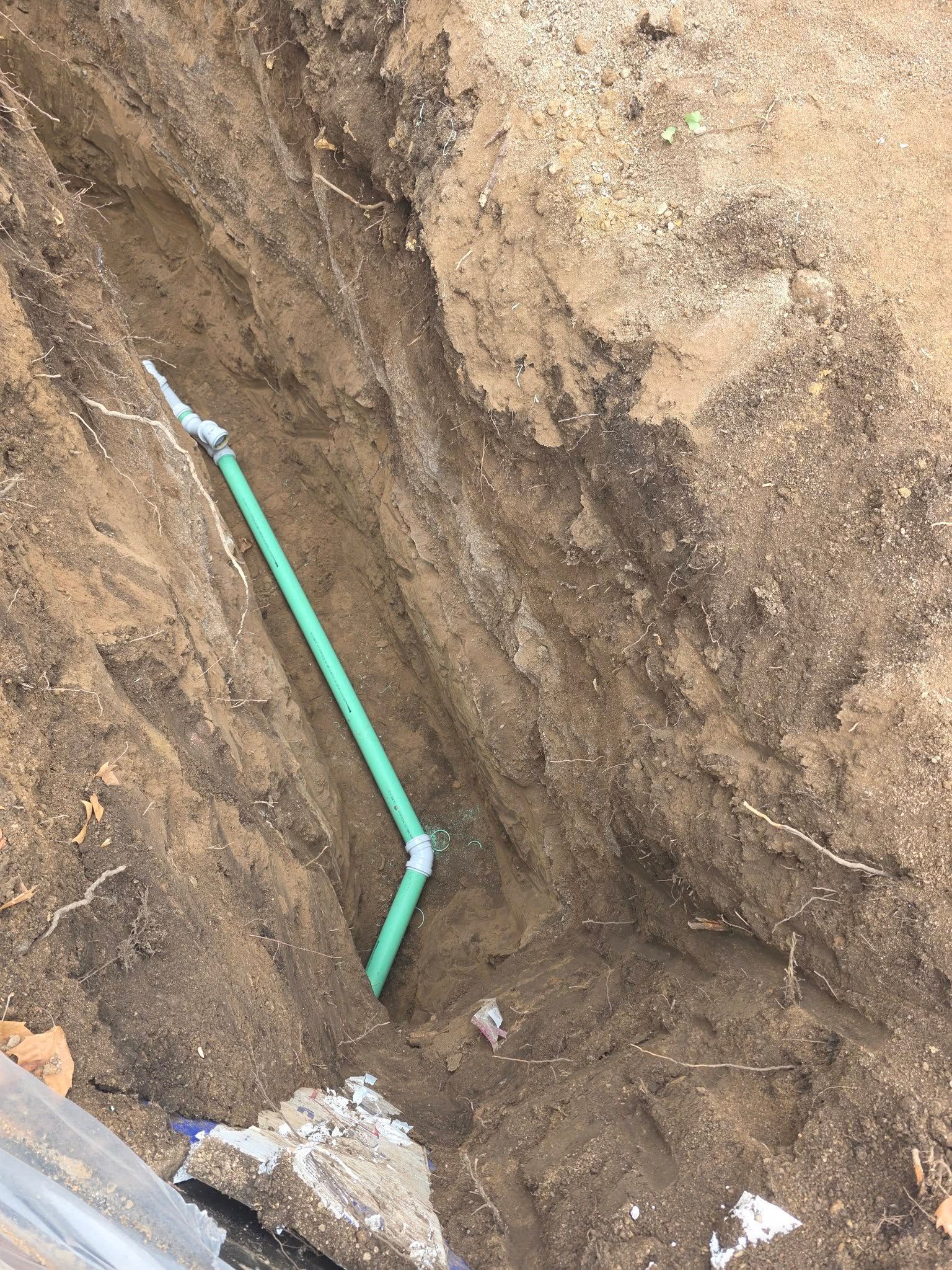 A green pipe with a 45-degree angle joint sits in a narrow dirt trench.
