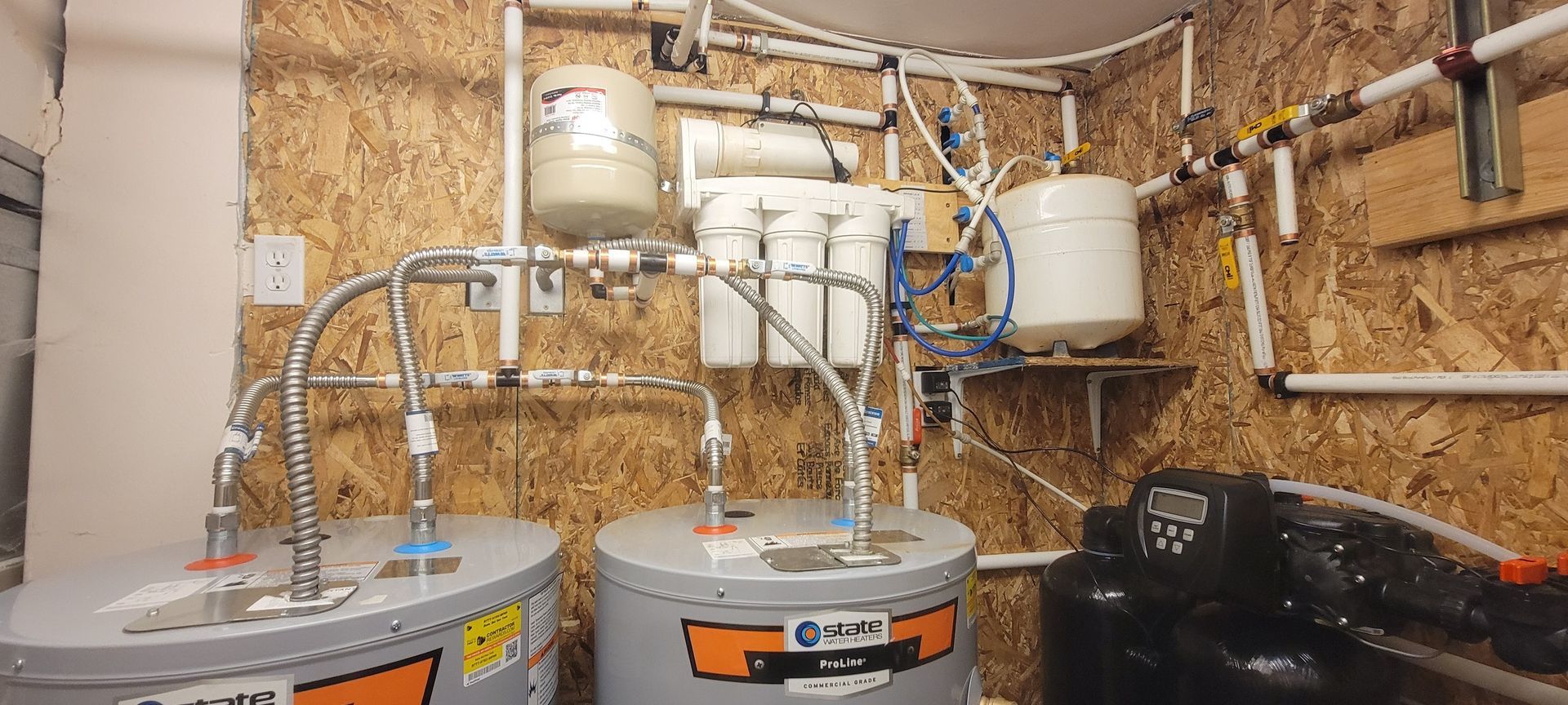 A mechanical room featuring water heaters, a multi-stage filtration system, and white piping on plywood walls.