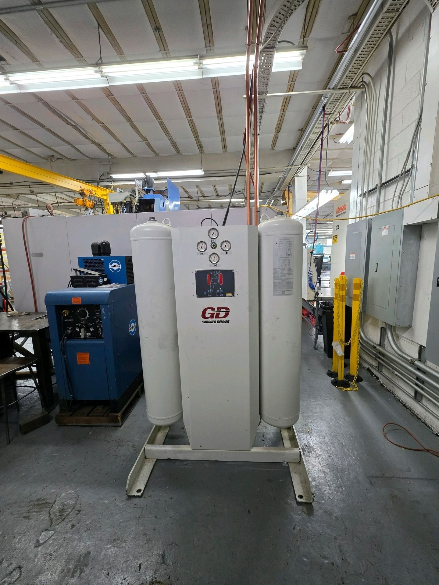A white compressed air dryer unit stands in an industrial workspace, with a blue machine visible to its left.