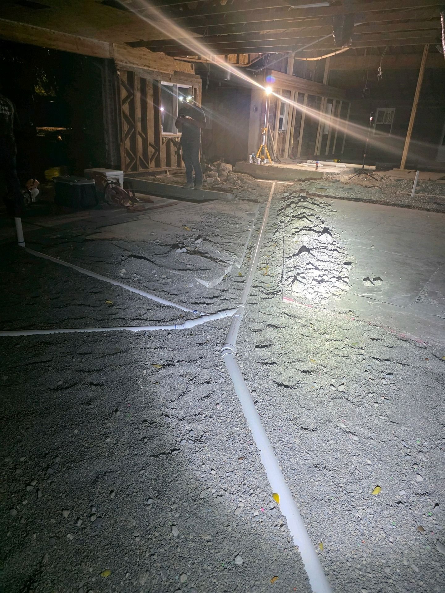 White PVC pipes for plumbing drainage laid across a gravel floor in a room undergoing construction.