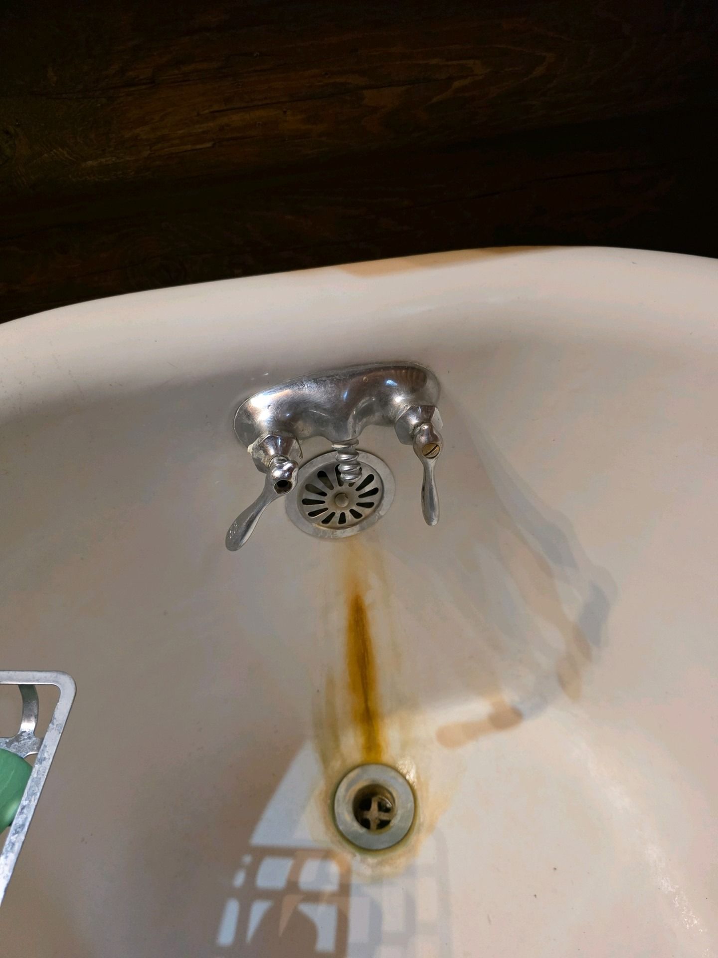 A bathtub with chrome fixtures and significant brown rust staining running down from the overflow drain to the floor drain.