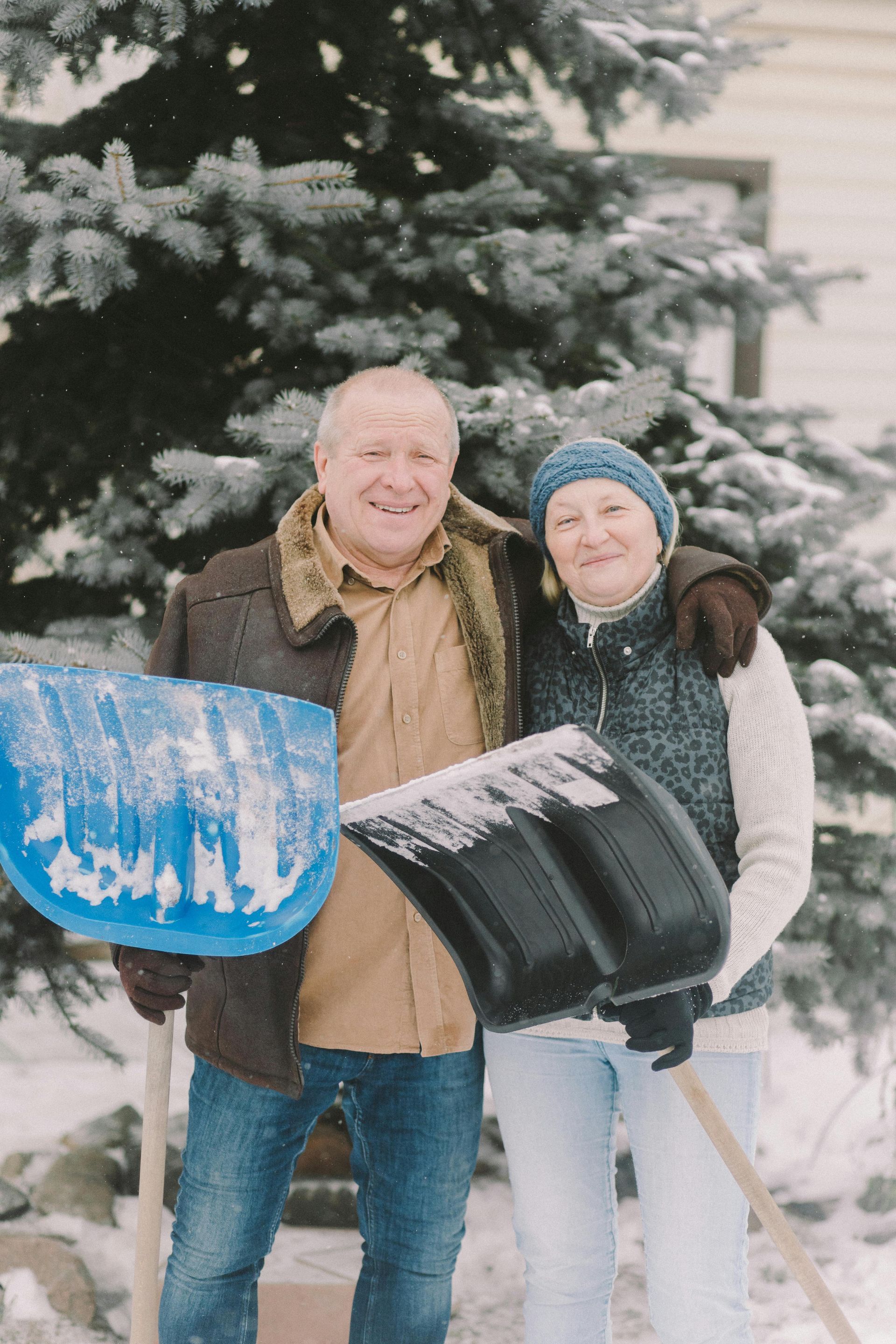 A man and a woman are standing next to each other in the snow holding snow shovels.