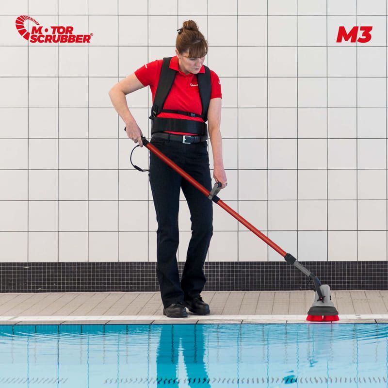 Woman wearing a red shirt and black pants uses a pool cleaning device to scrub a swimming pool's edge.