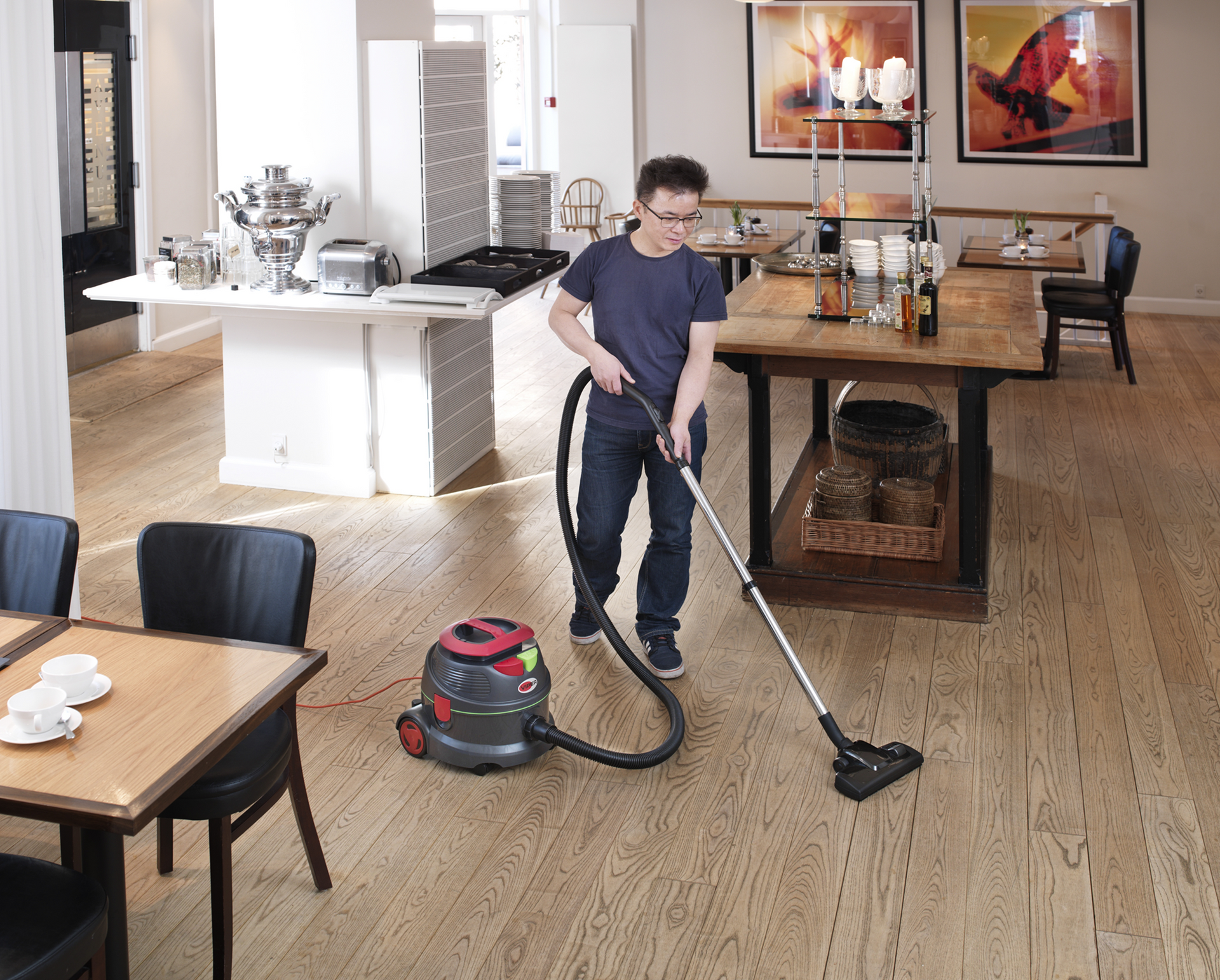 Person vacuums a wooden floor in a cafe/restaurant setting.
