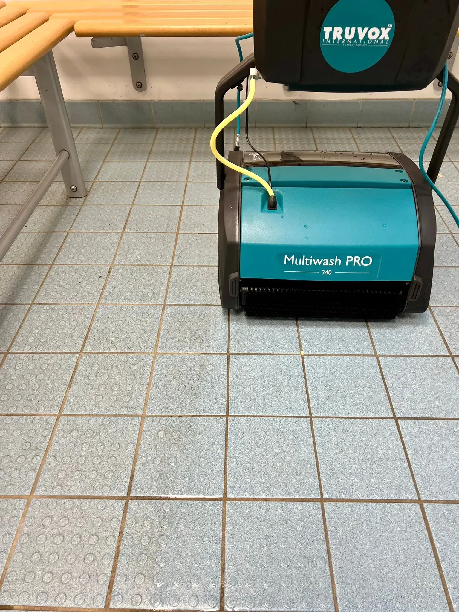 Person using a teal and black Truvox Multiwash PRO floor cleaning machine near a pool. 