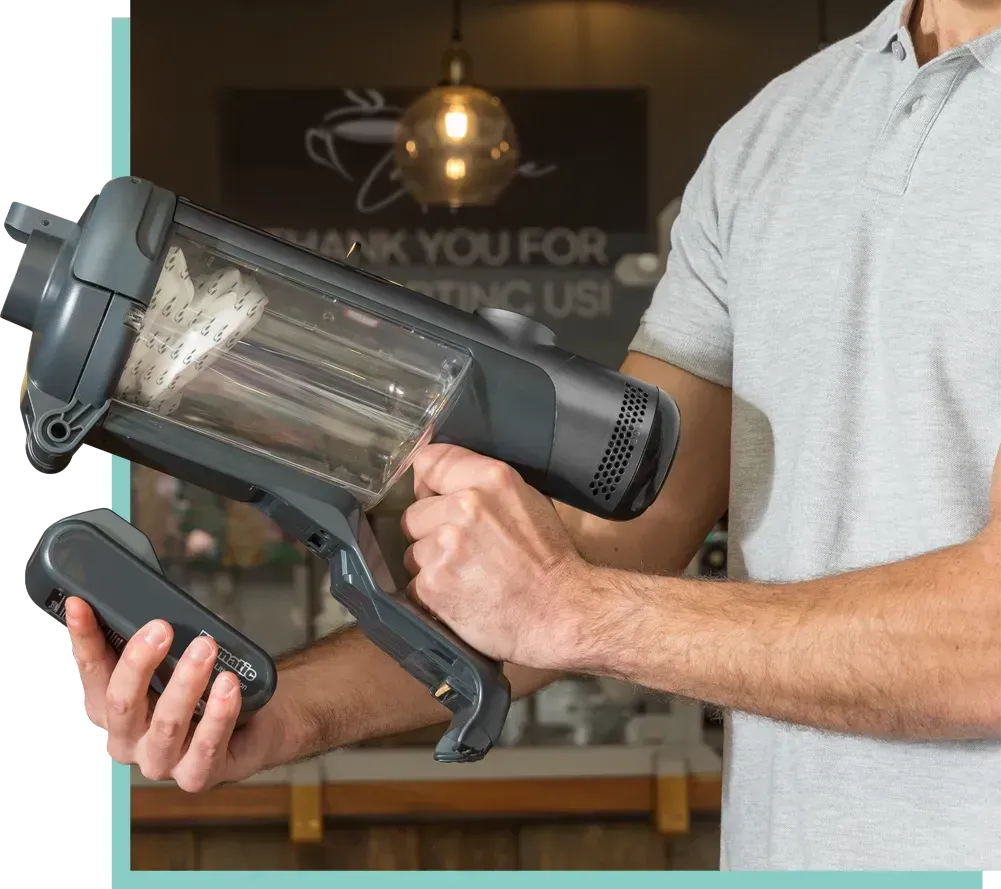 Man uses a handheld vacuum to clean a counter covered in crumbs in a bar.
