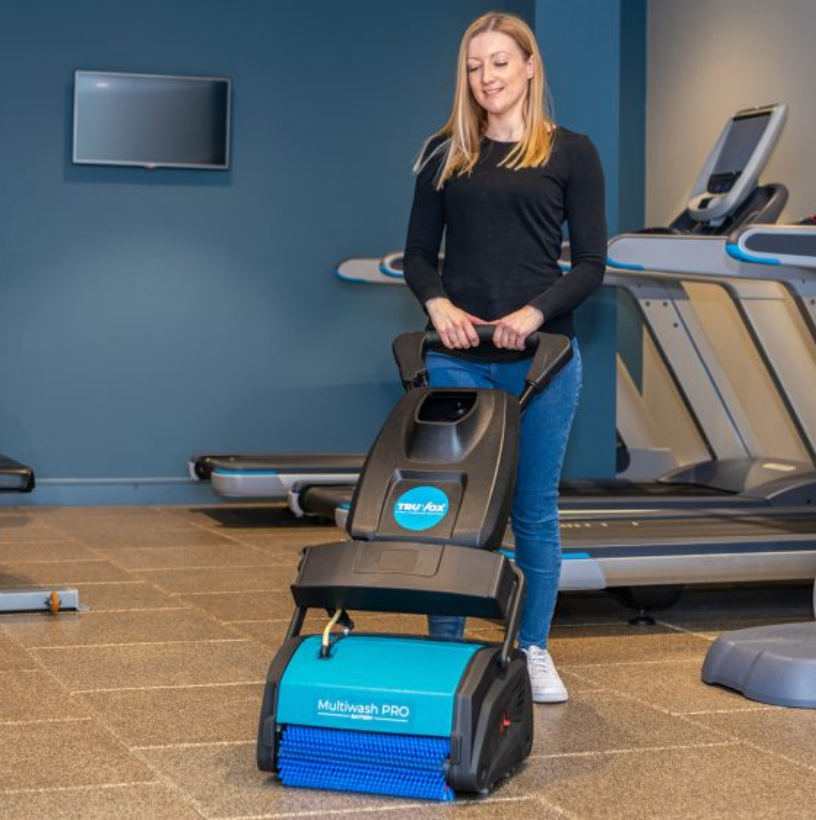 Person operating a teal and black floor cleaner labeled 