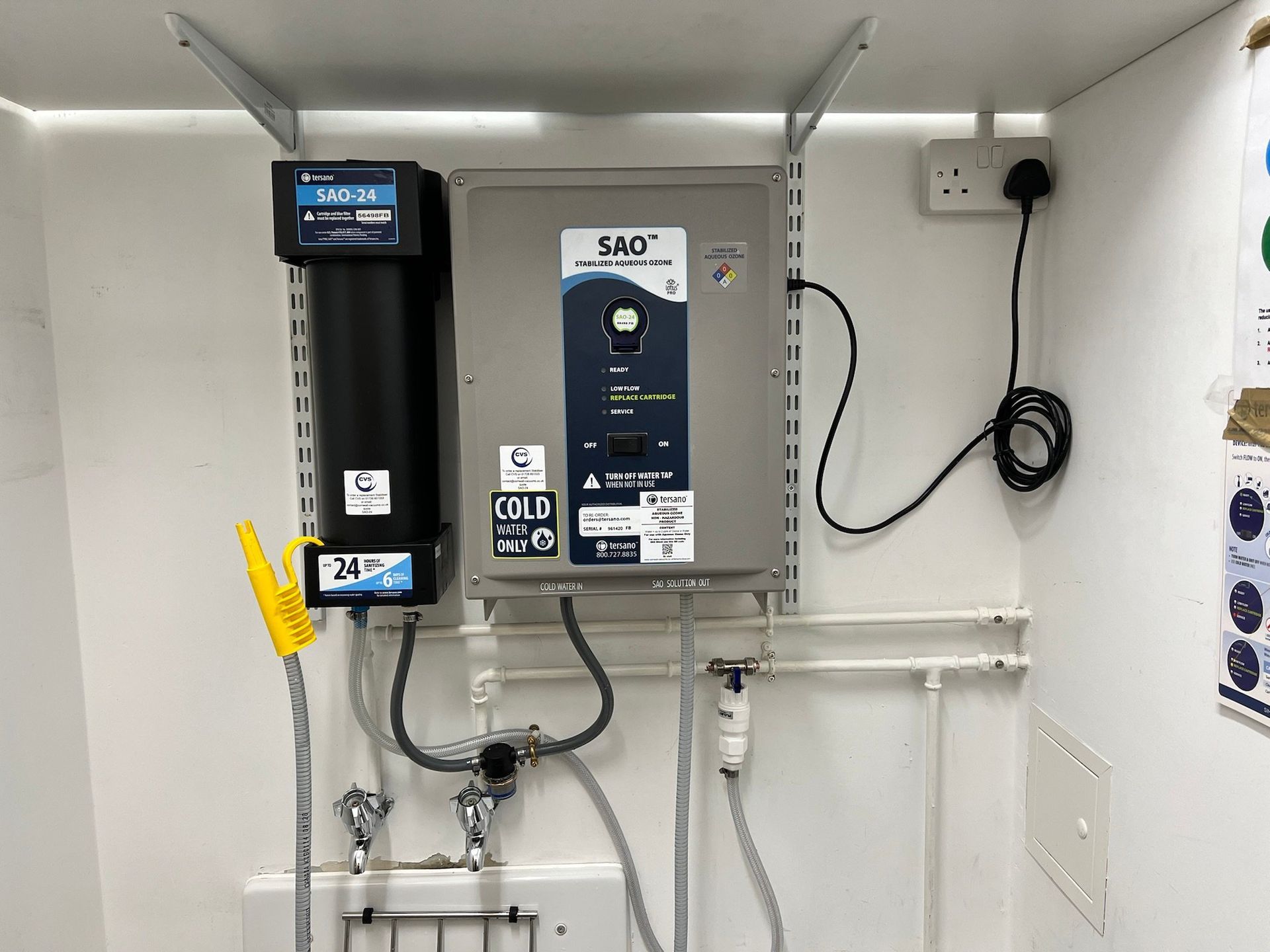 Medical equipment panel mounted on a white wall. Includes a filter, control box, and faucet.