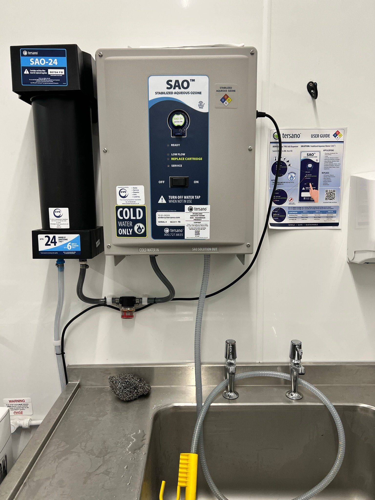 Water filtration system mounted above a stainless steel sink, with digital displays and attached hoses.