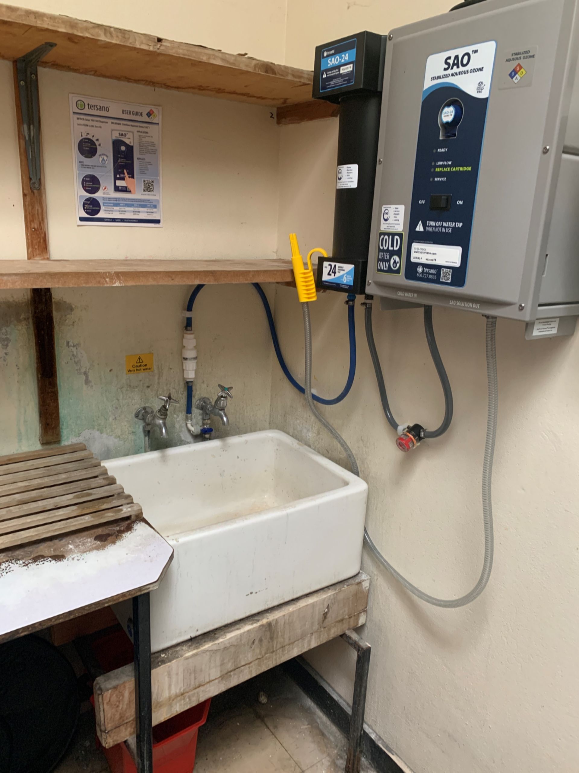 A utility sink with plumbing, water heater, and a water filter under wooden shelving.