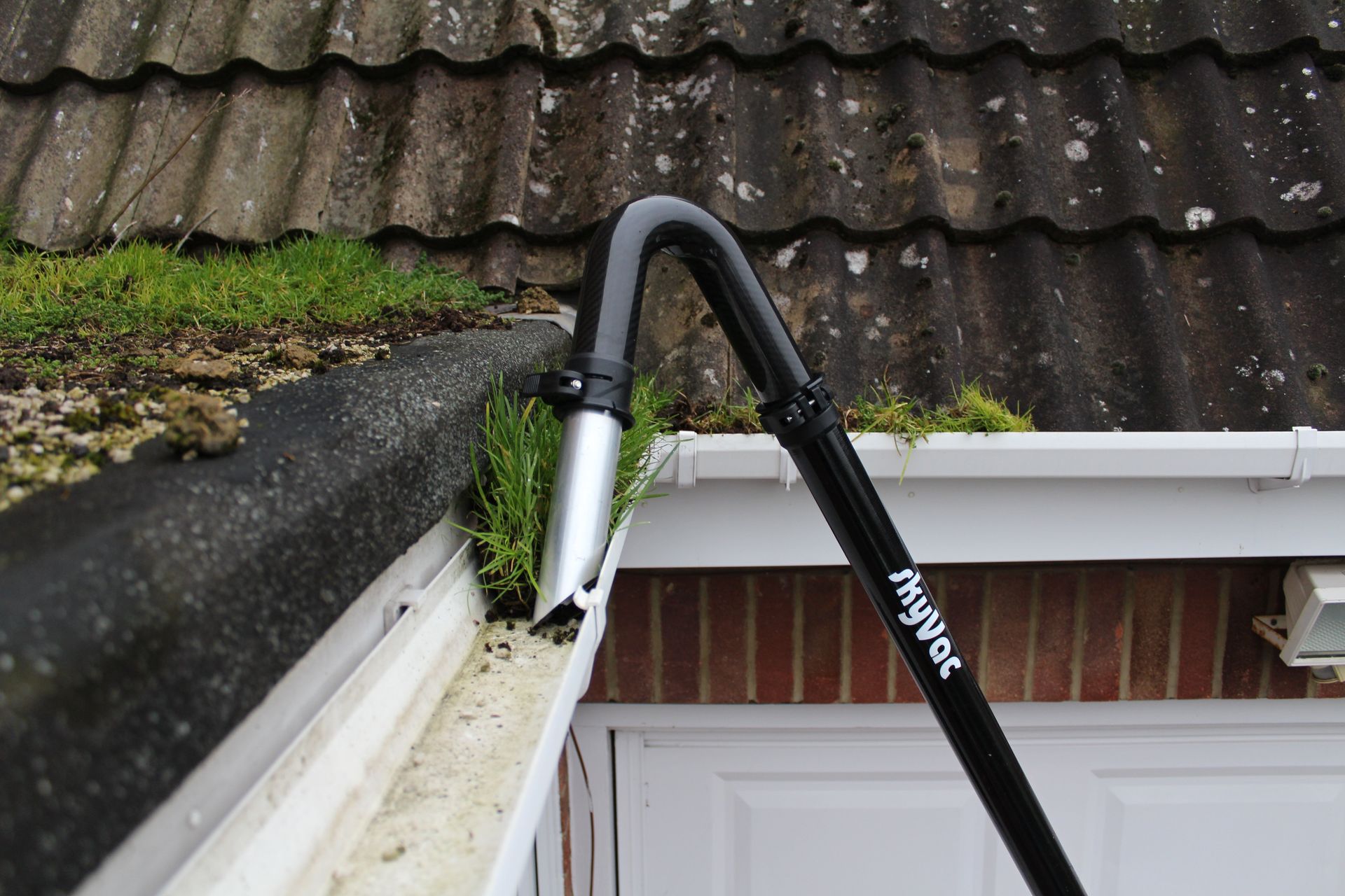 Black gutter cleaning tool removing debris from a gutter on a house roof.