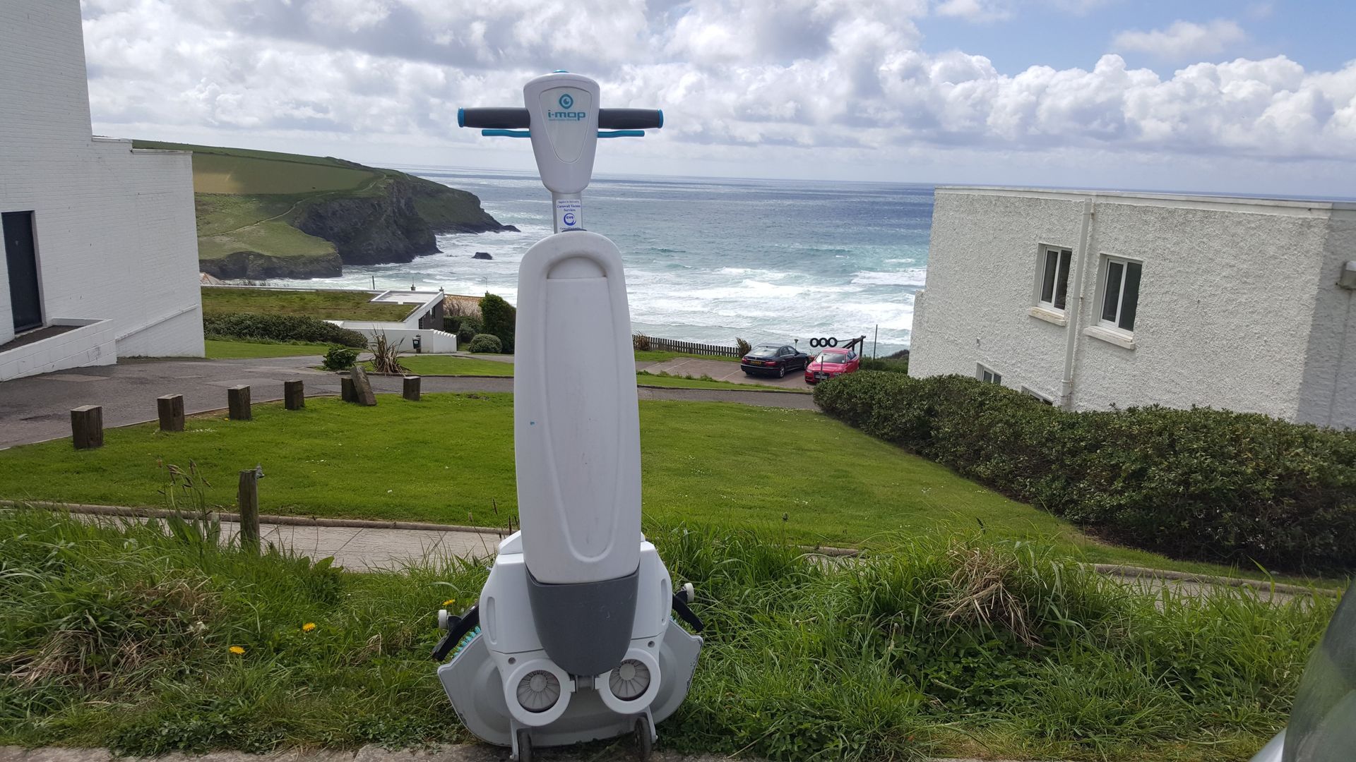A white robot on a grassy hill overlooking the ocean. The sky is cloudy.