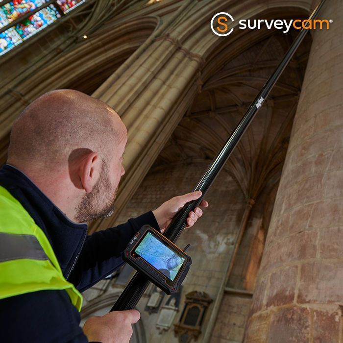 Man using a pole camera to inspect the inside of a building. He is wearing a reflective vest.