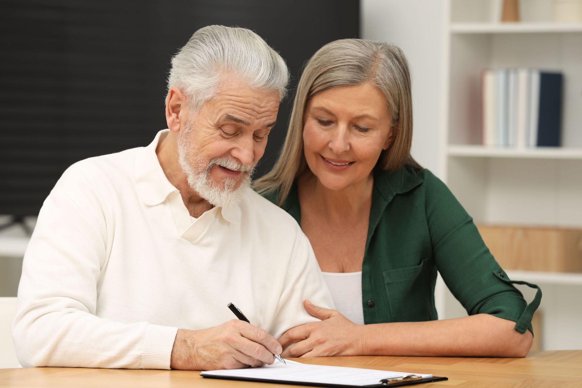 An elderly couple is sitting at a table signing a document.