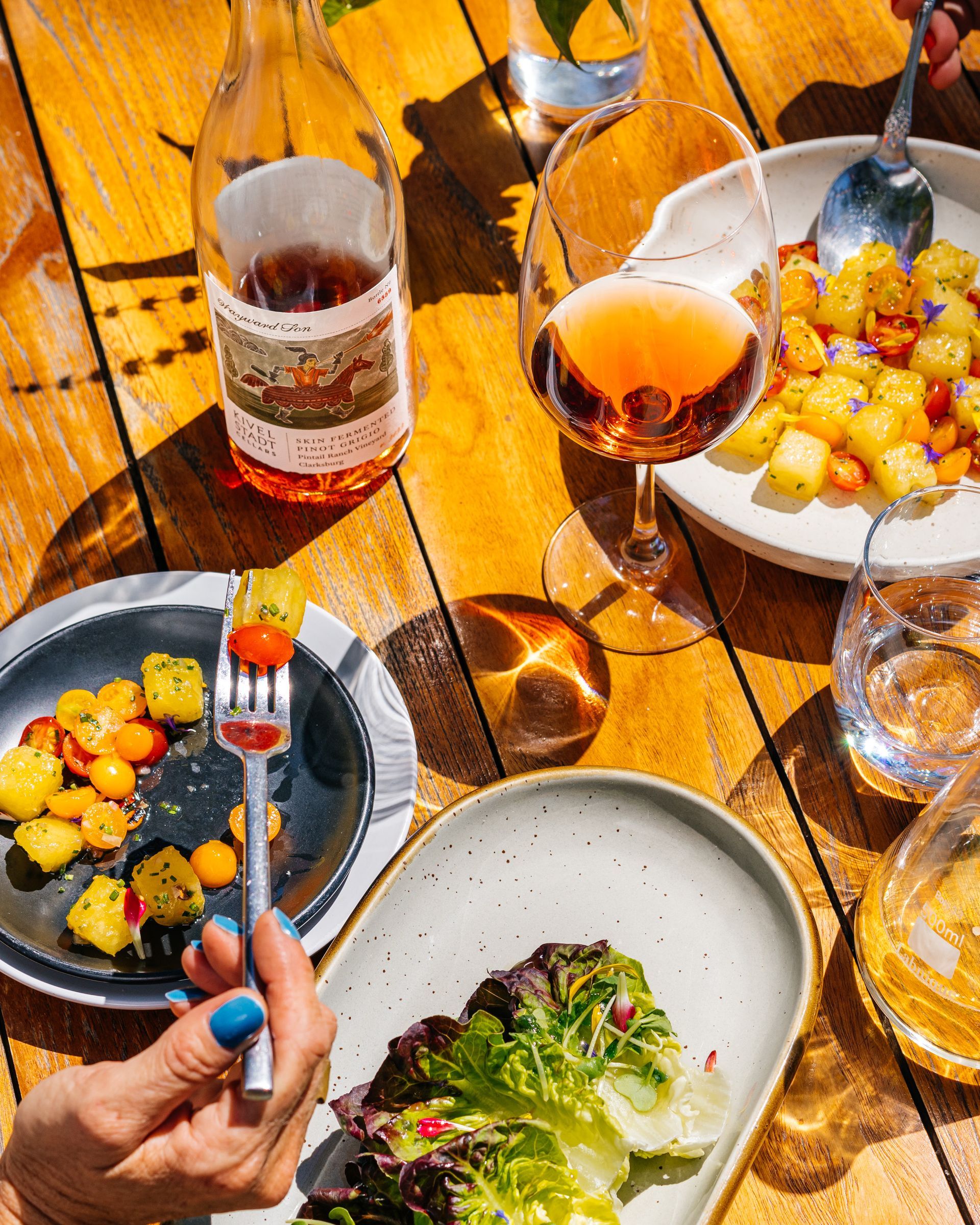 A person is holding a fork over a plate of food on a wooden table.
