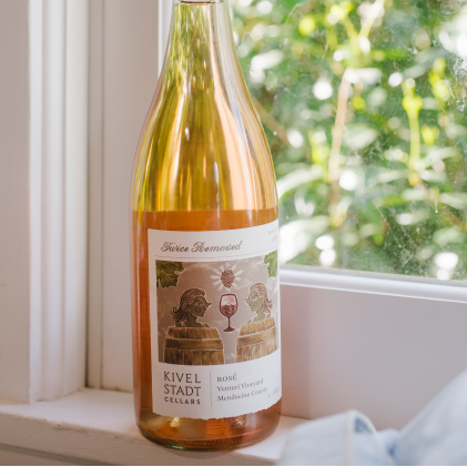 A bottle of wine is sitting on a window sill.