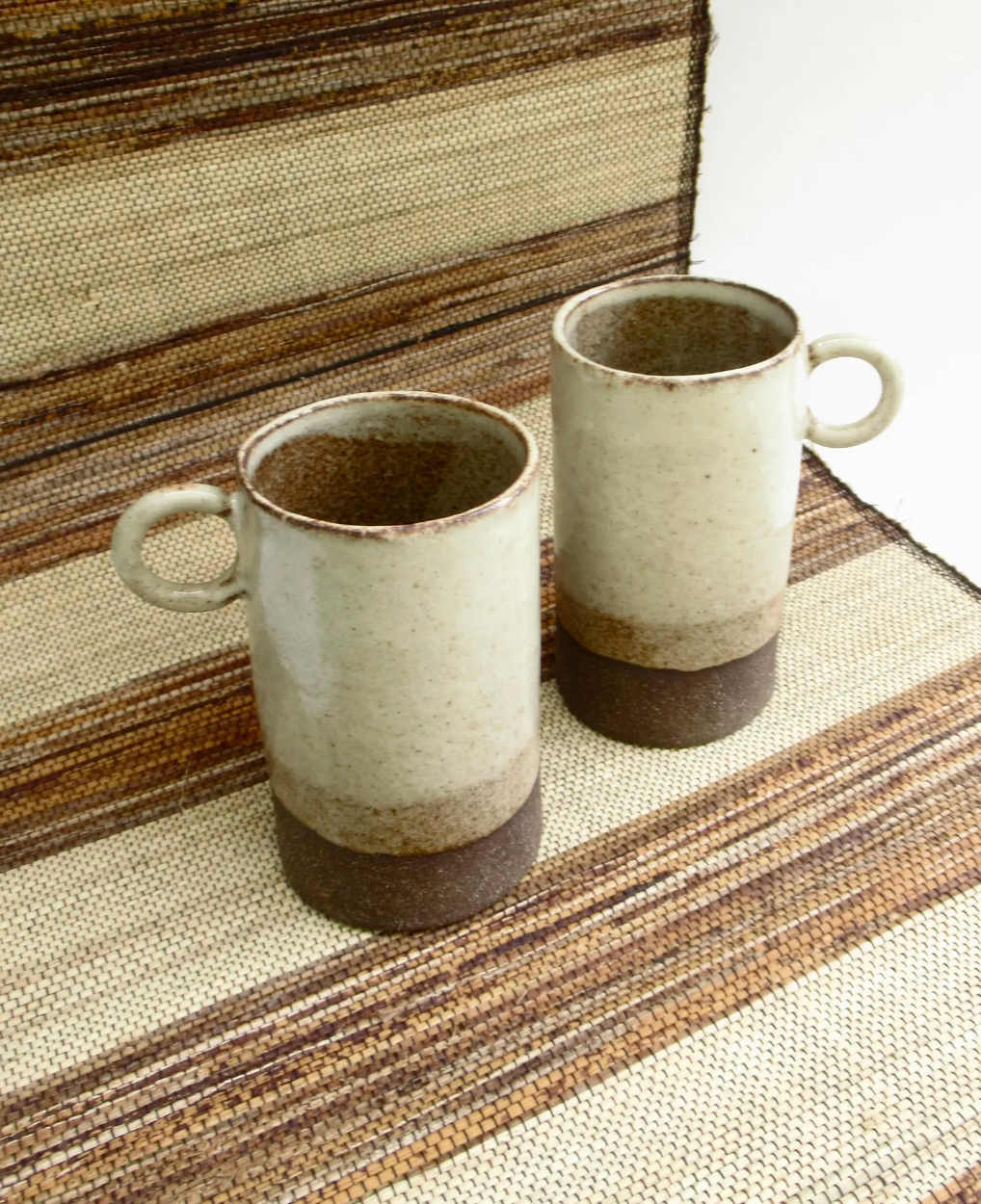 Two mugs are sitting on a striped table cloth