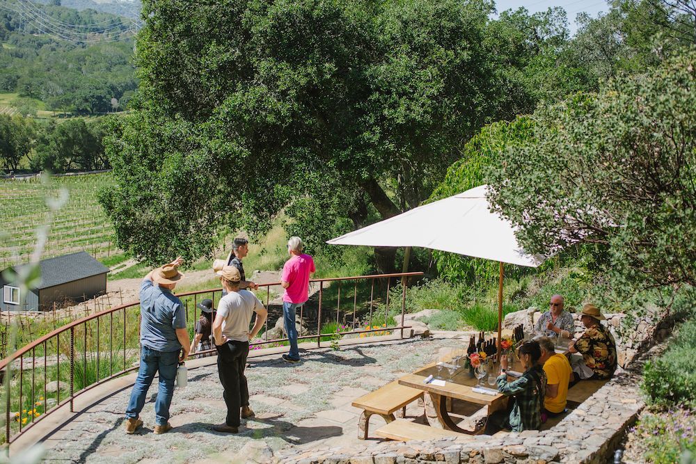 A group of people are sitting at a table under an umbrella on a patio.