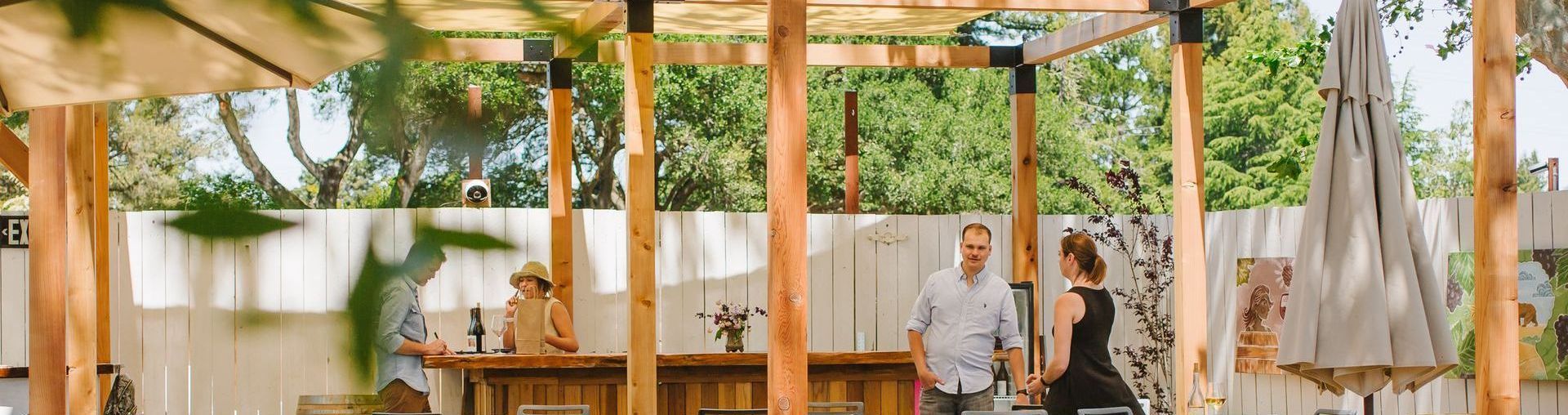 A man and a woman are standing under a wooden pergola in a restaurant.