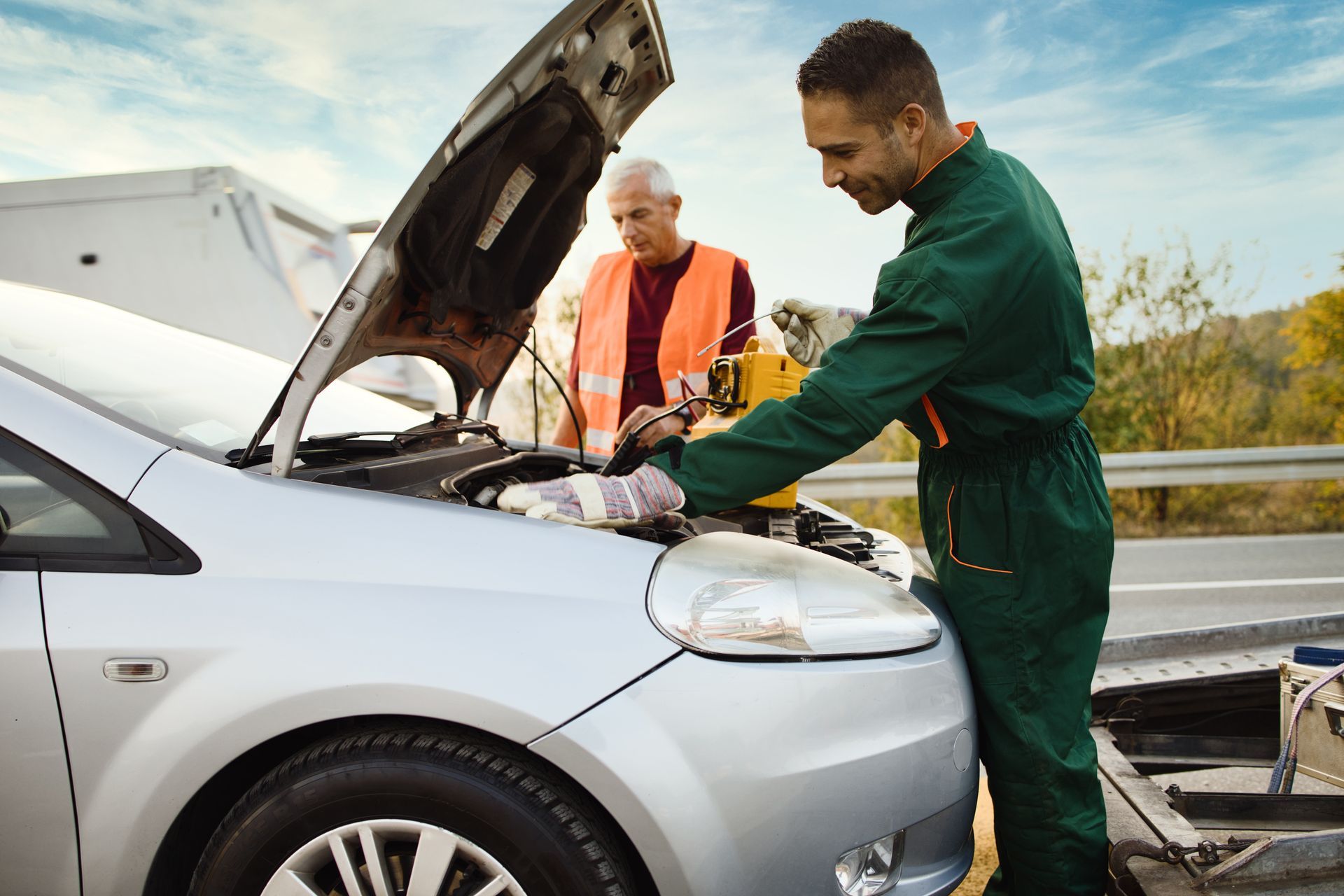 Two men are working on a broken down car on the side of the road.