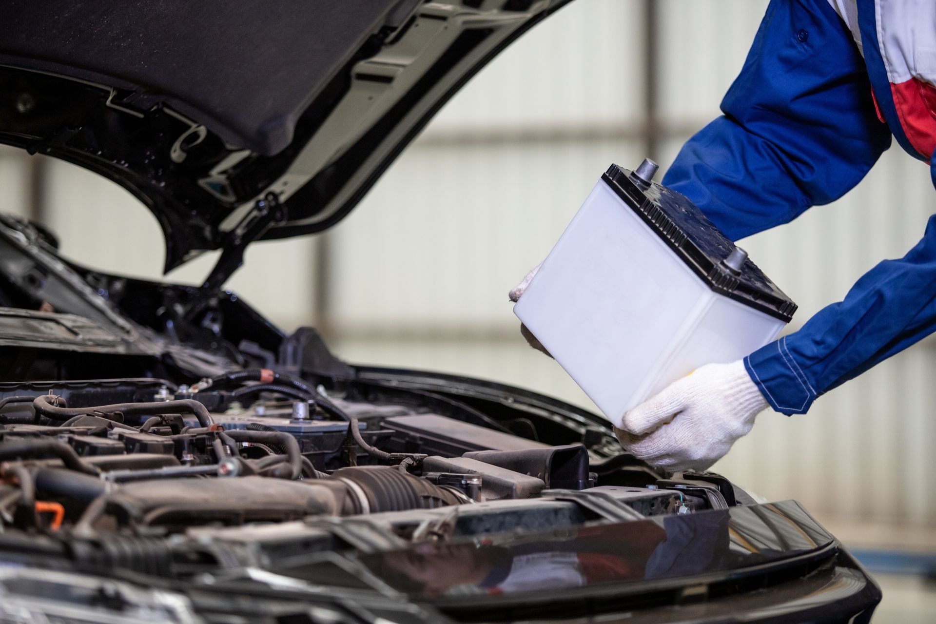 A mechanic is changing a car battery in a garage.
