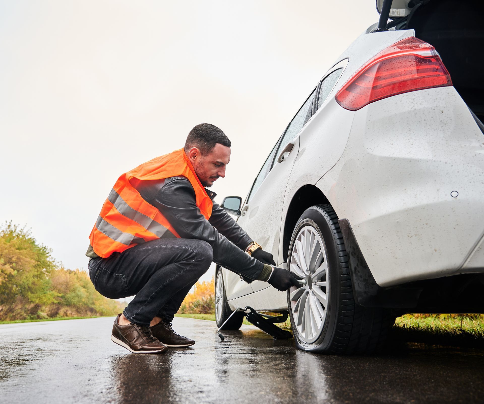 A man is changing a tire on a car on the side of the road.