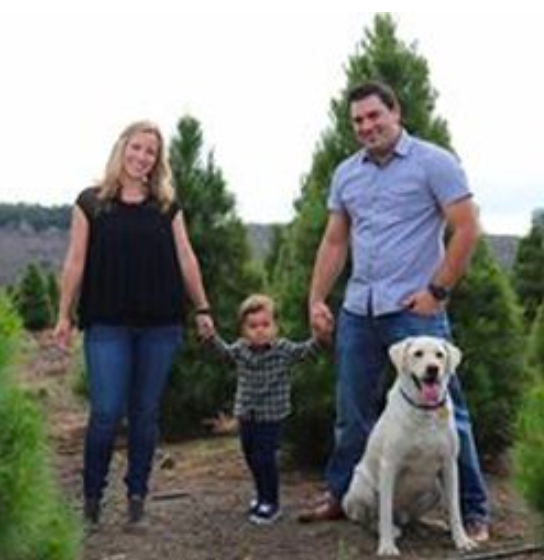 a family is posing for a picture in front of a Christmas tree farm .