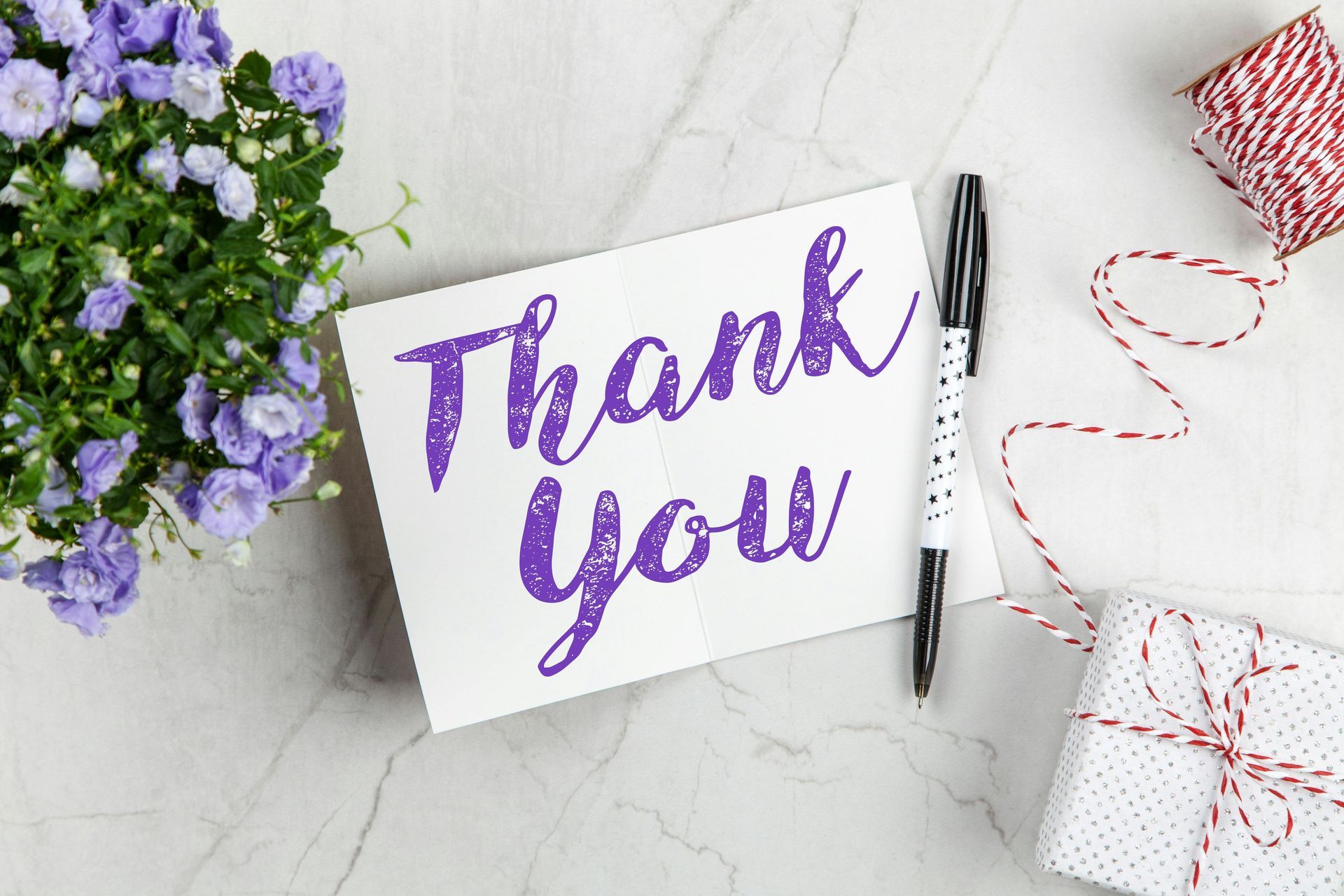 A thank you card is sitting on a table next to a pen and flowers.