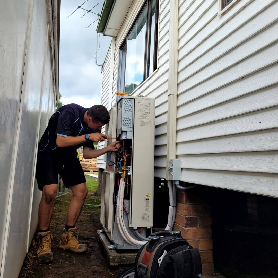 Technician Working on Outdoor Electrical Unit Beside a House — Alpine Refrigeration & Air Conditioning Pty Ltd in Wollongong, NSW