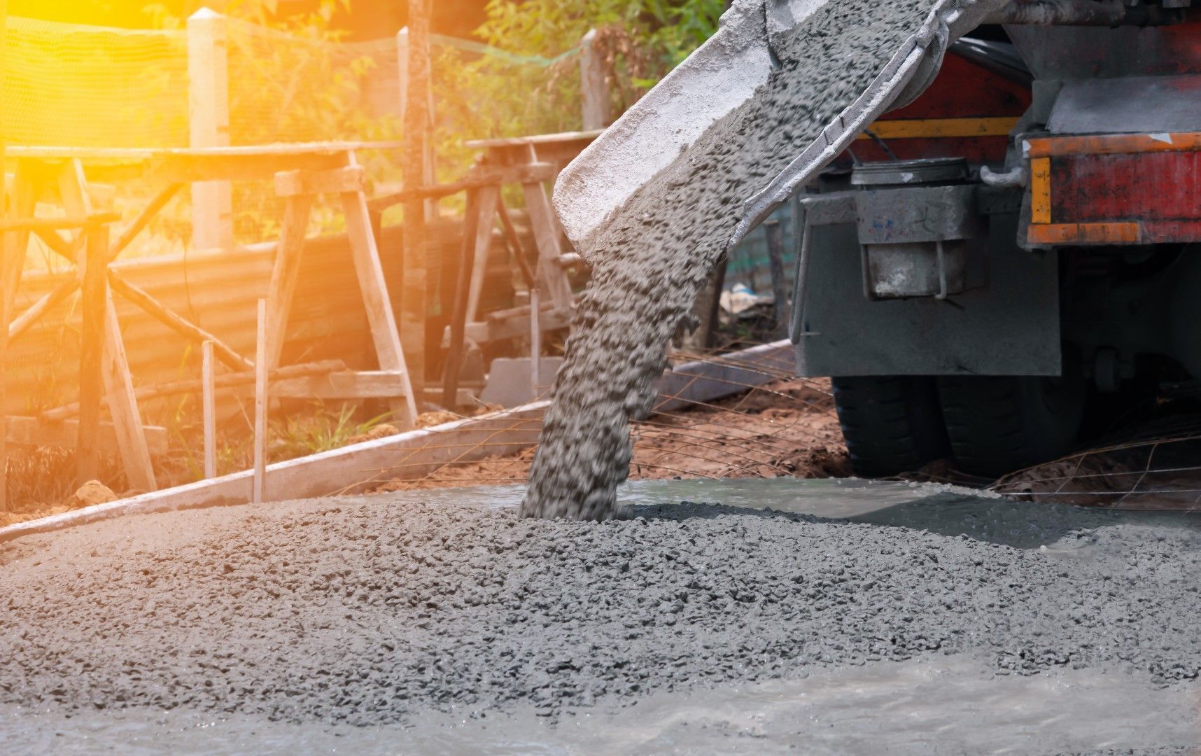 Cement pouring from a truck chute onto a ground surface, construction site, sunny.