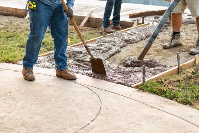 Workers spreading wet concrete in a wooden form with shovels, constructing a walkway outdoors.