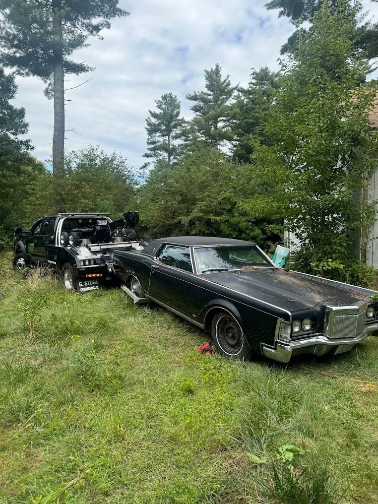 A black car is being towed by a tow truck in a grassy field.