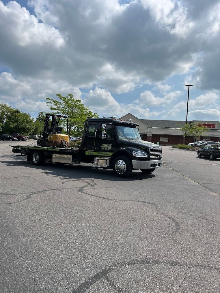 A tow truck with a forklift on the back is parked in a parking lot.