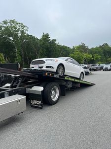 A white car is being towed by a tow truck.