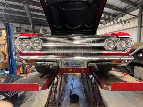 A red car with the hood up is on a lift in a garage.
