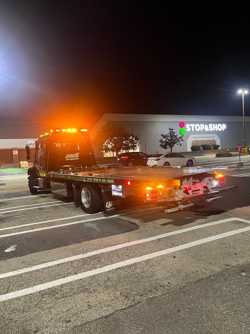 A tow truck is towing a car in a parking lot at night.