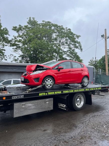 A red car is sitting on top of a tow truck.