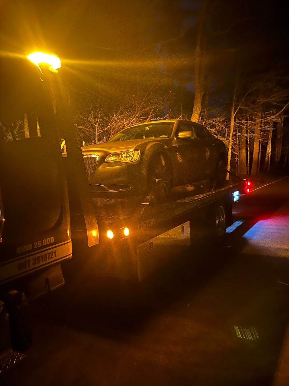 A car is being towed by a tow truck at night.