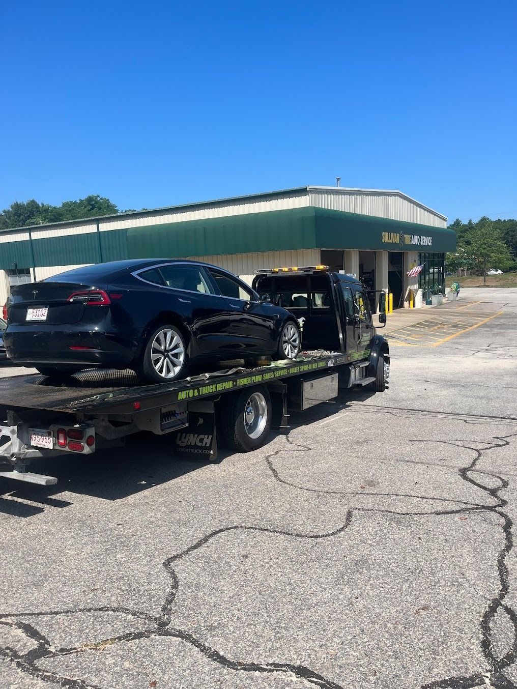 A black car is being towed by a tow truck.