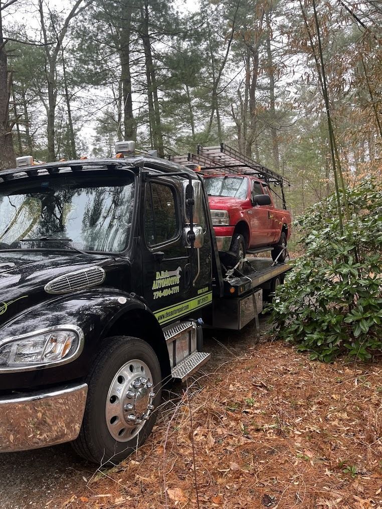 A black tow truck is towing a red truck in the woods.