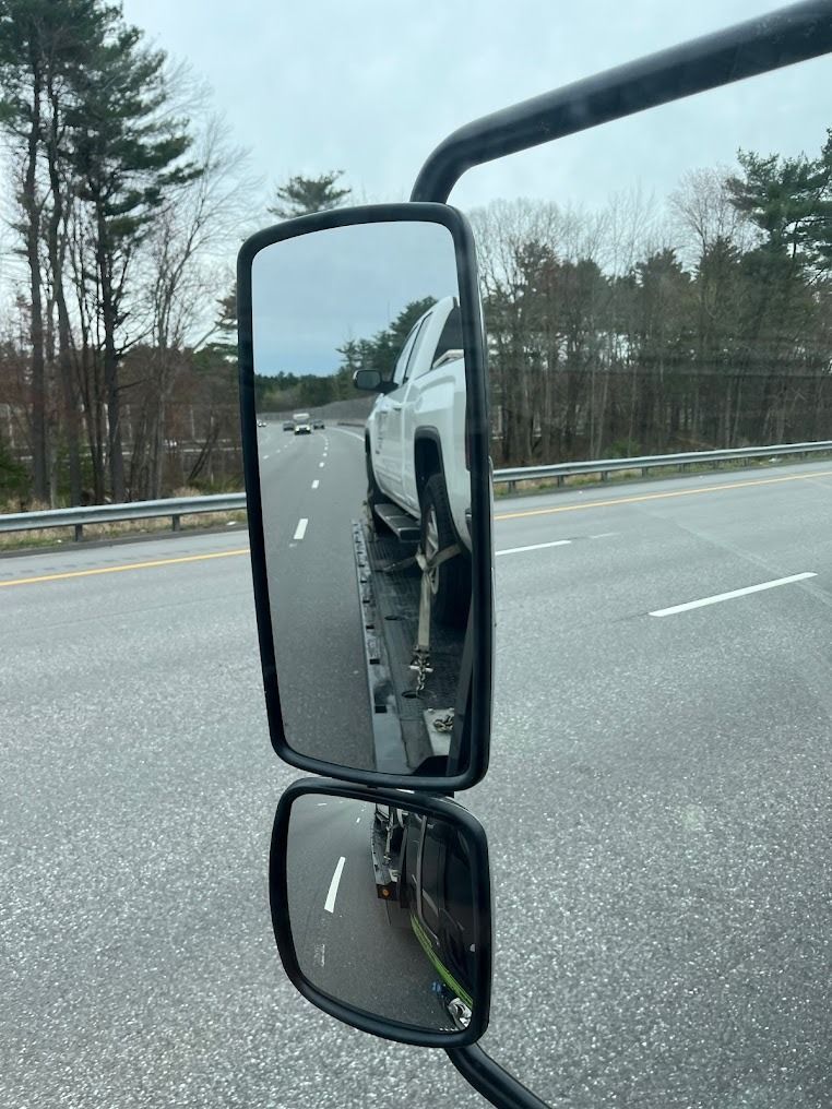 A truck is reflected in a side view mirror on a highway.