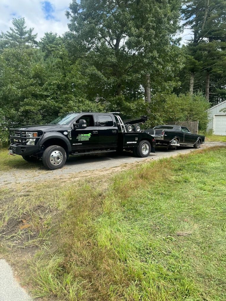 A black tow truck is towing a black car down a dirt road.